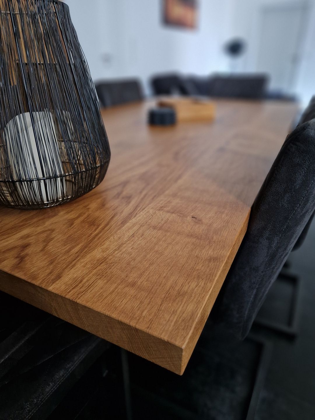 Holztisch mit Dekoration und dunklen Polsterstühlen im Hintergrund.